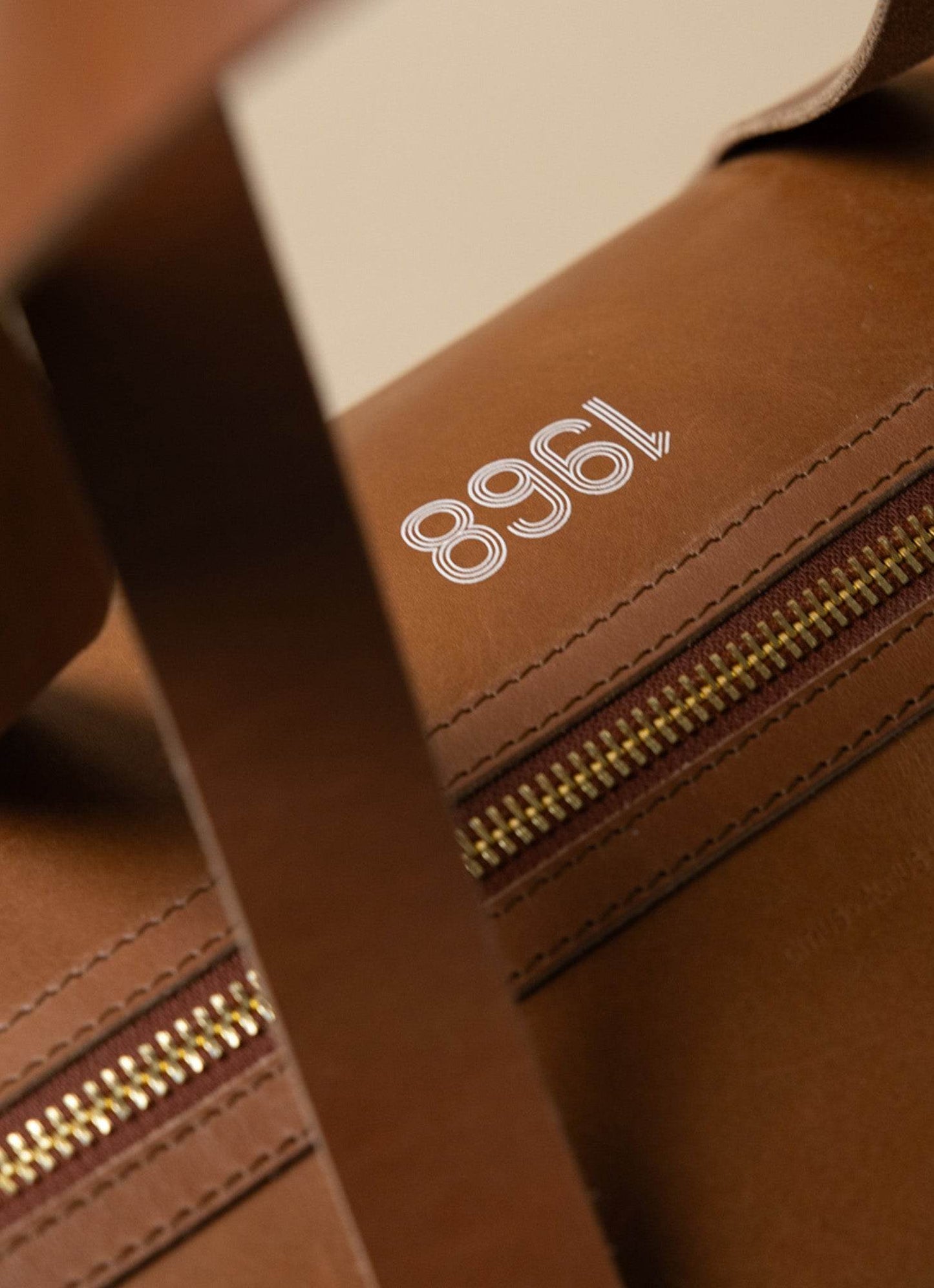 Close-up of brown leather bag with gold zipper and white '1968' logo, men's lifestyle accessory