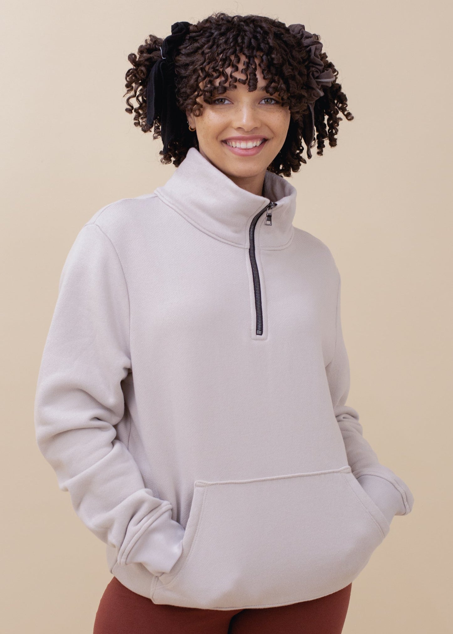 Woman wearing oatmeal half-zip sweatshirt with kangaroo pocket, neutral background