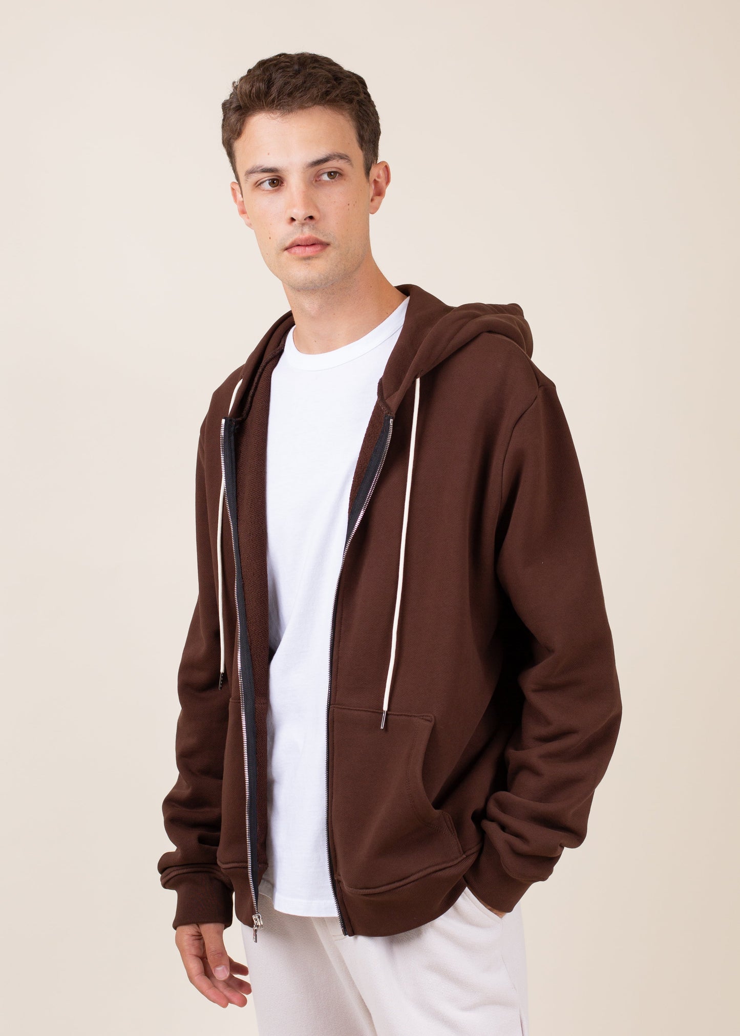 Man in brown zip-up hoodie and white T-shirt, casual men's fashion on cream background