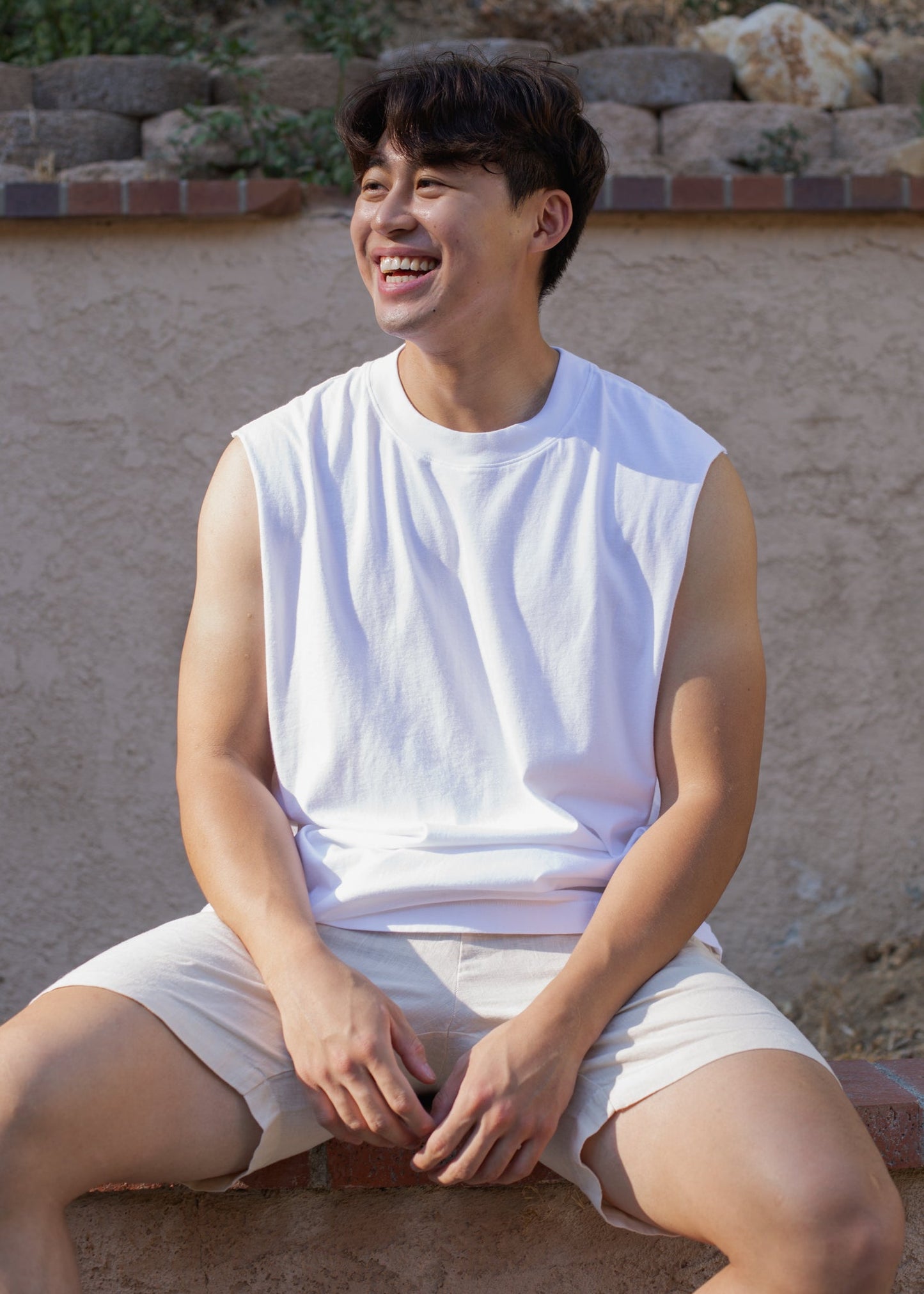 Smiling man wearing a white muscle tank and beige shorts, outdoor casual fashion for men