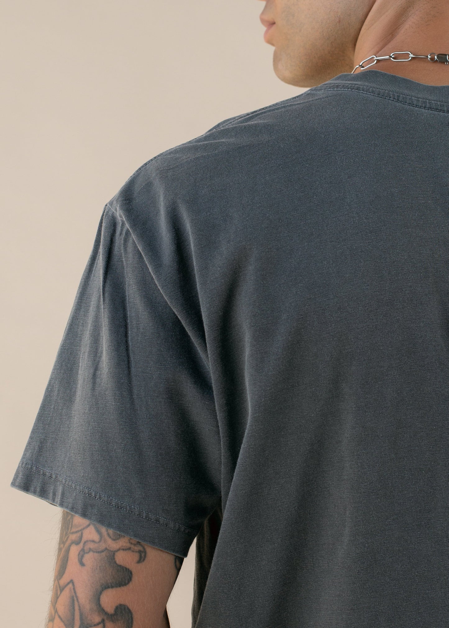 Man wearing a dark grey t-shirt, silver chain, and visible tattoo, stylish menswear fashion