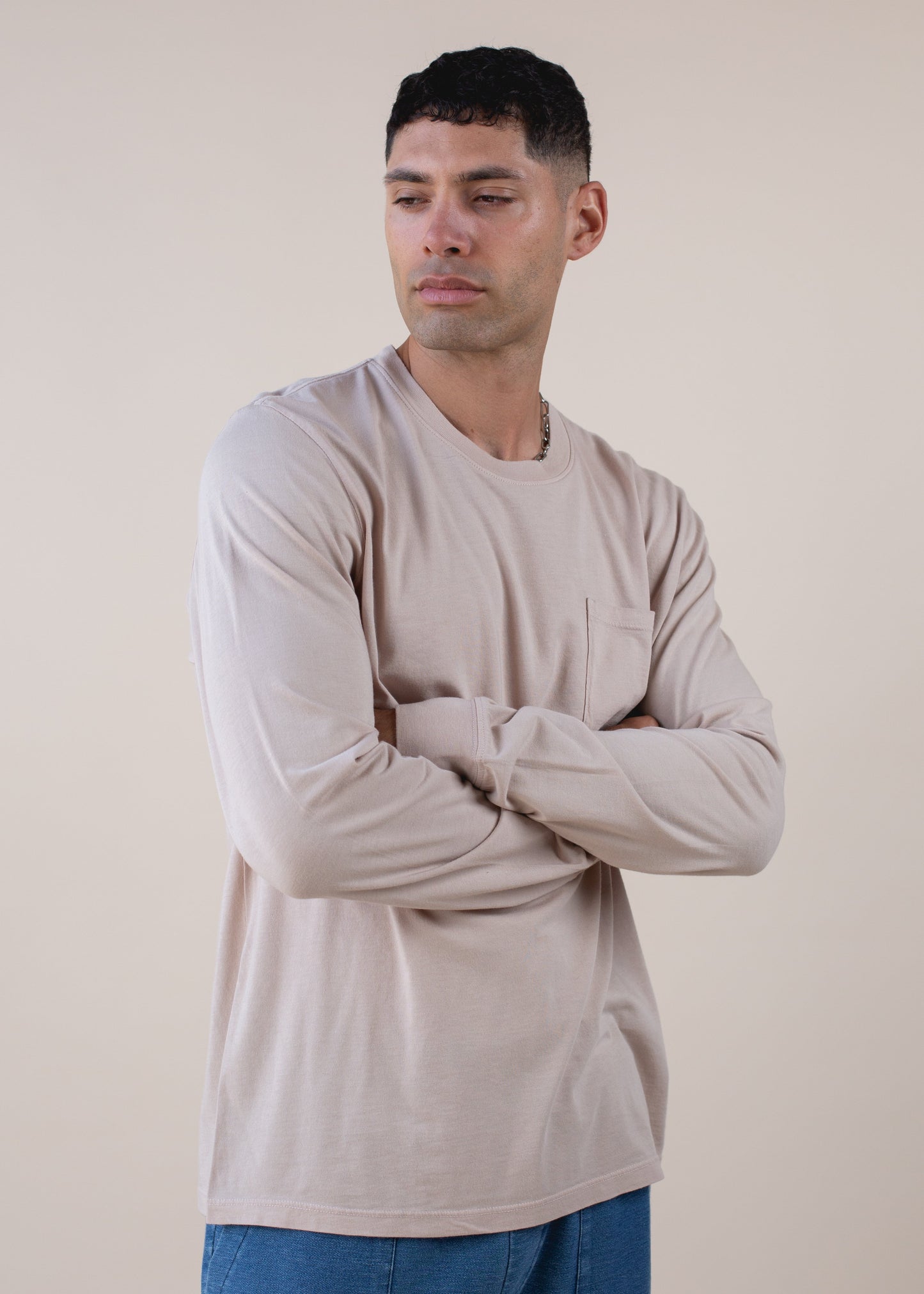 Man modeling a beige long sleeve shirt and blue jeans against a neutral background