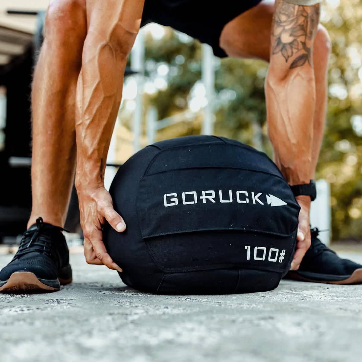Man lifting GORUCK 100 lb sandbag outdoors, fitness gear for men's workout lifestyle