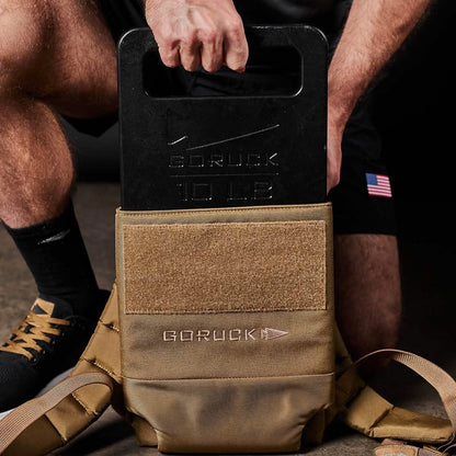 Man loading 10 lb GORUCK weight plate into tan tactical backpack, fitness gear for men