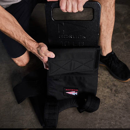 Man loading 10 lb GORUCK weight plate into black tactical vest on gym floor