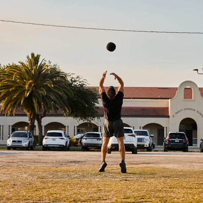 Man outdoors throwing medicine ball, athletic workout in front of cars and palm tree, Mann marketplace fitness lifestyle