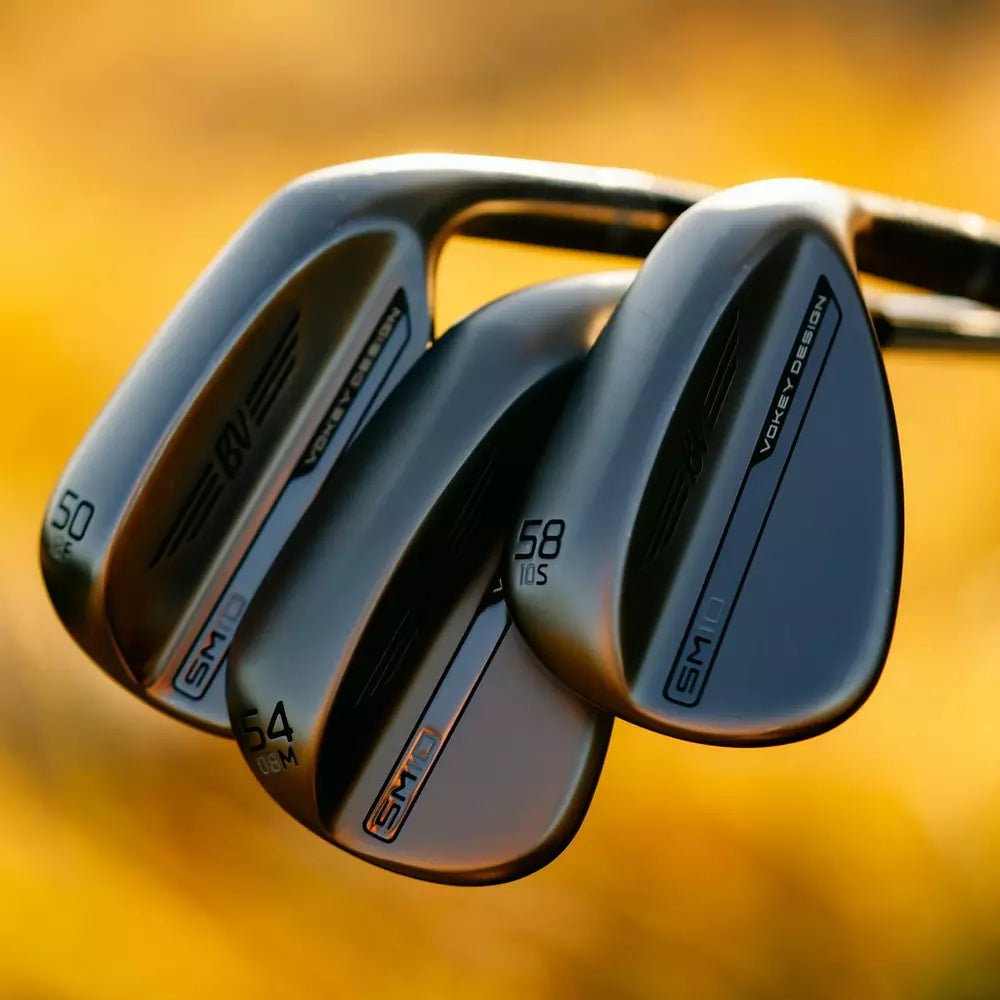 Close-up of three Vokey Design SM10 golf clubs with metallic finish, outdoor setting