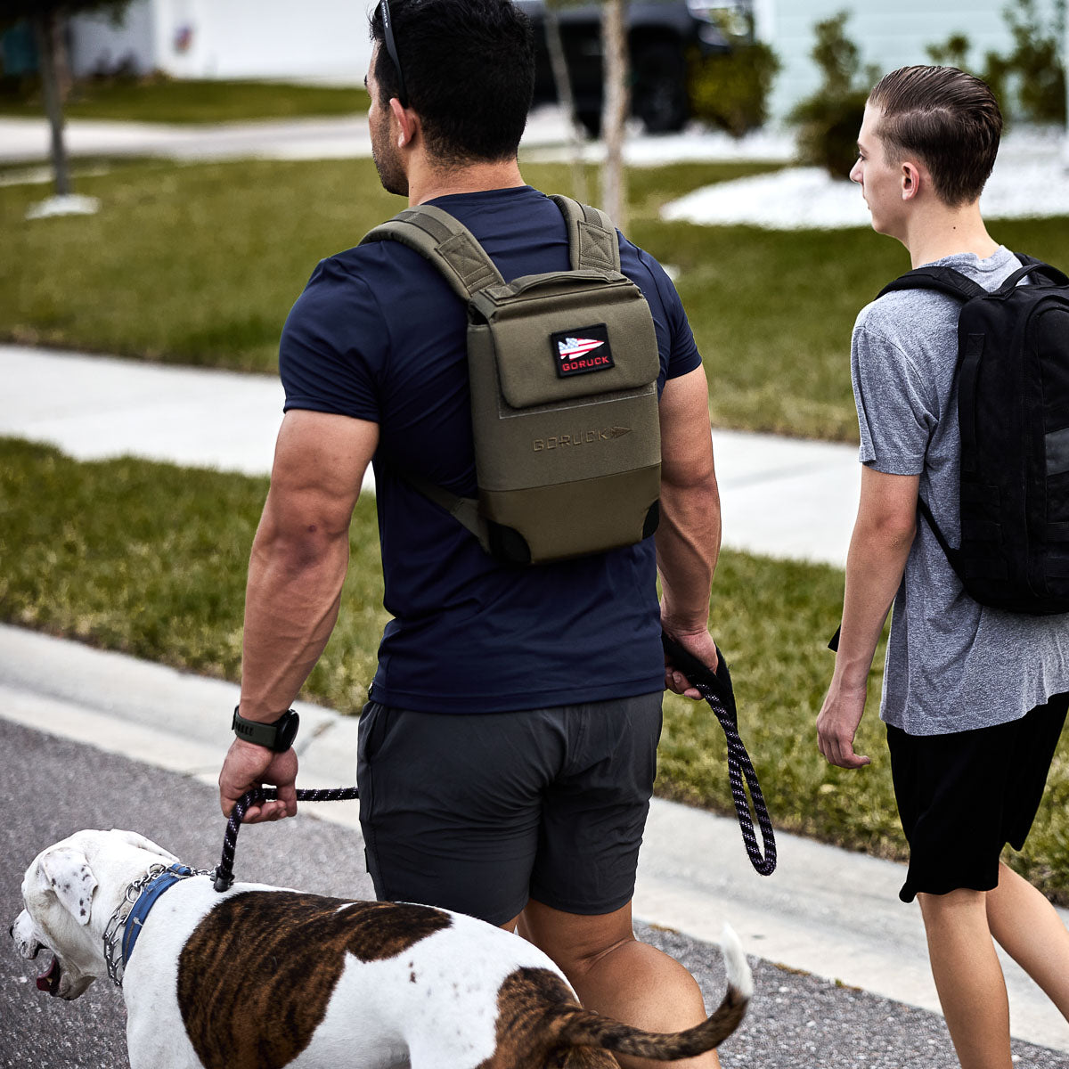 Man with fitness backpack walking dog alongside teen boy outdoors, active lifestyle