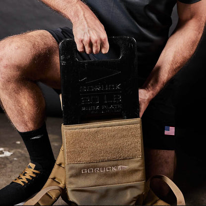 Man placing 20 LB GORUCK ruck plate into tan backpack, fitness gear for men's workouts