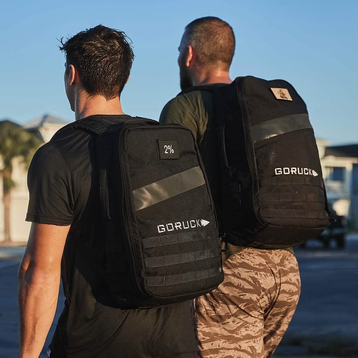 Two men outdoors wearing black GORUCK backpacks, active lifestyle, men's fitness gear.