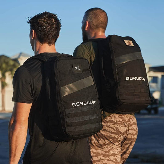 Two men outdoors wearing black GORUCK backpacks, active lifestyle, men's fitness gear.