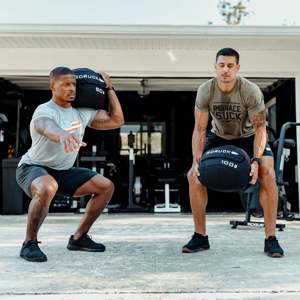Two men in athletic wear doing outdoor functional training with weighted sandbags