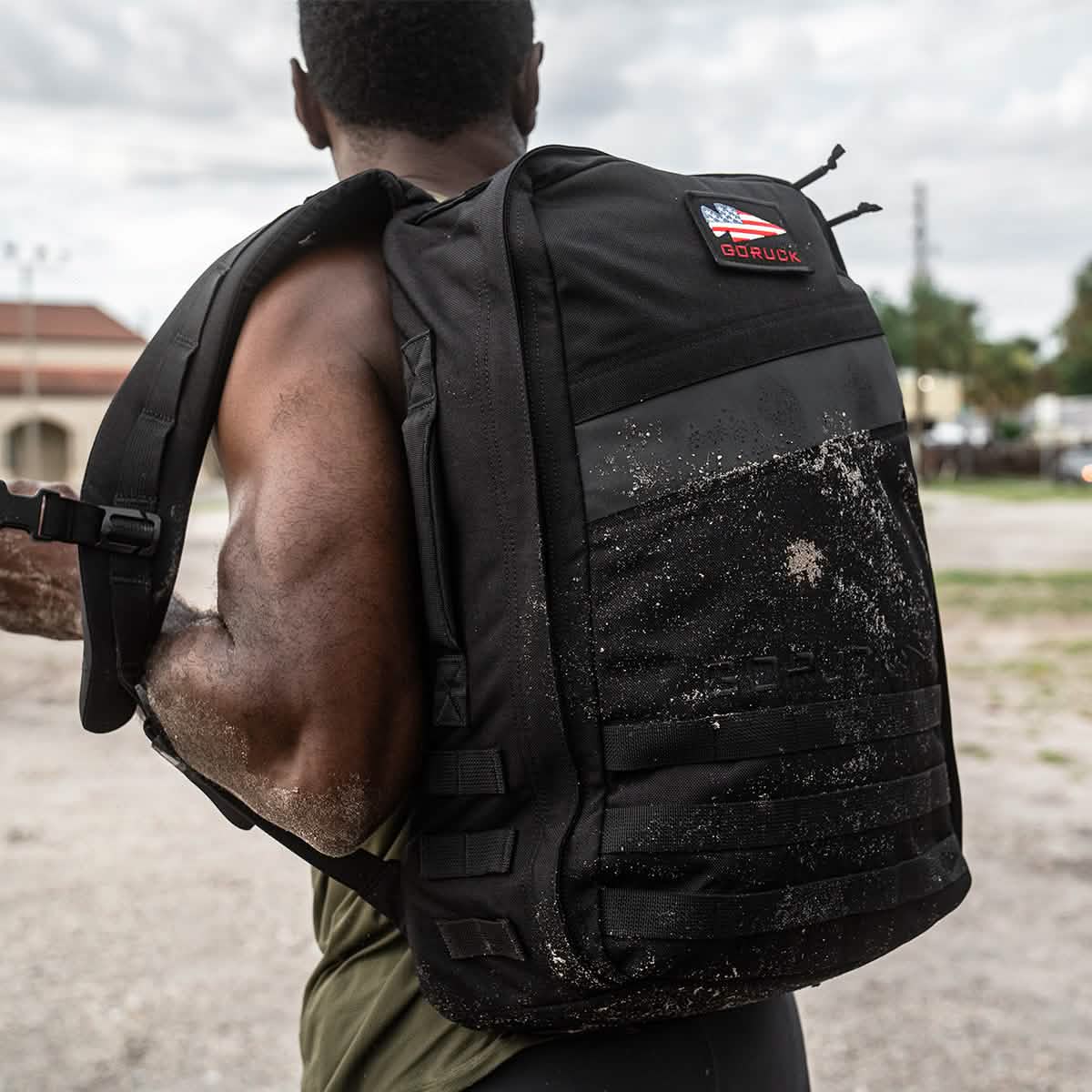 Man carrying black GORUCK backpack outdoors, showcasing rugged, athletic lifestyle gear