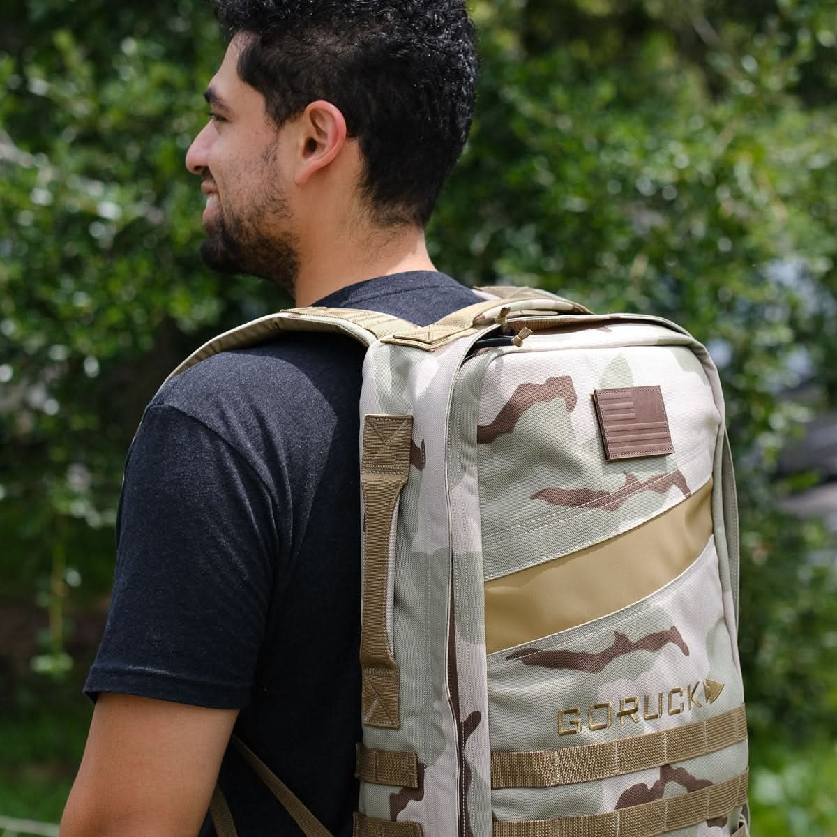 Man outdoors wearing GORUCK camo backpack, masculine style, men’s lifestyle accessory