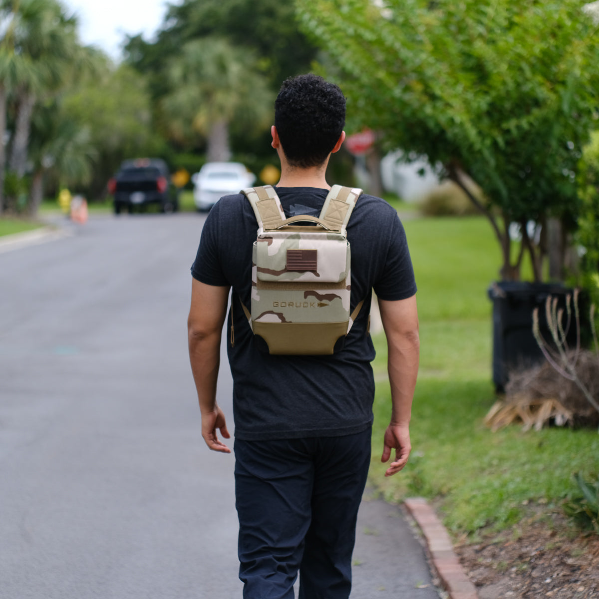 Man walking outdoors wearing a camouflage GORUCK backpack, casual street style