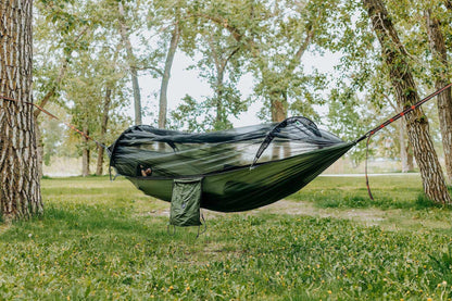 Lightweight hammock with mosquito net in a forest setting for outdoor comfort.