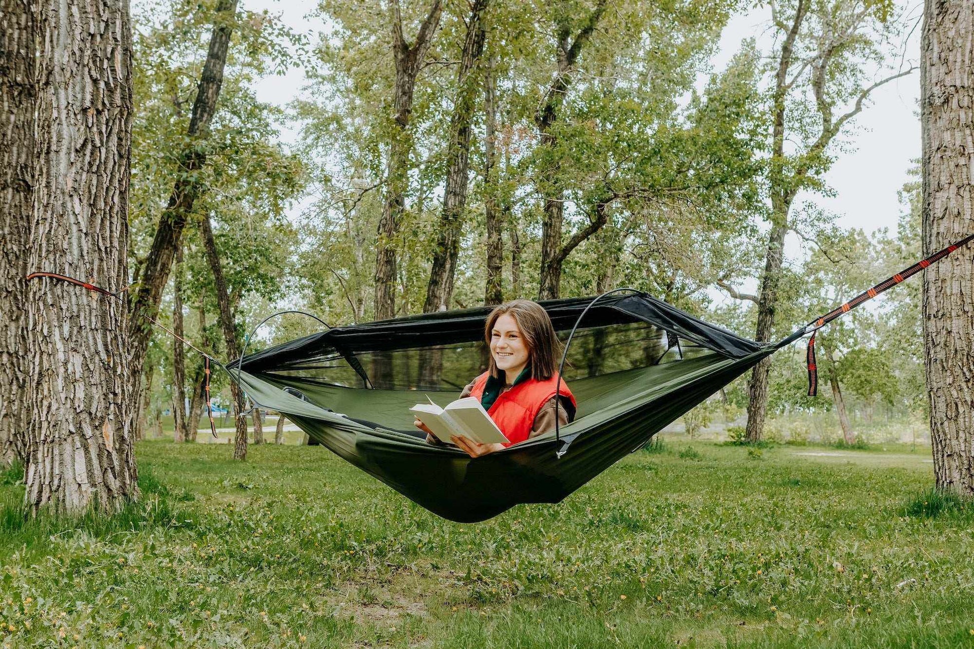 Hammock with mosquito net in a wooded area, person relaxing while reading.