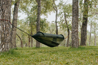 Lightweight hammock with mosquito net suspended between trees in a forest setting.