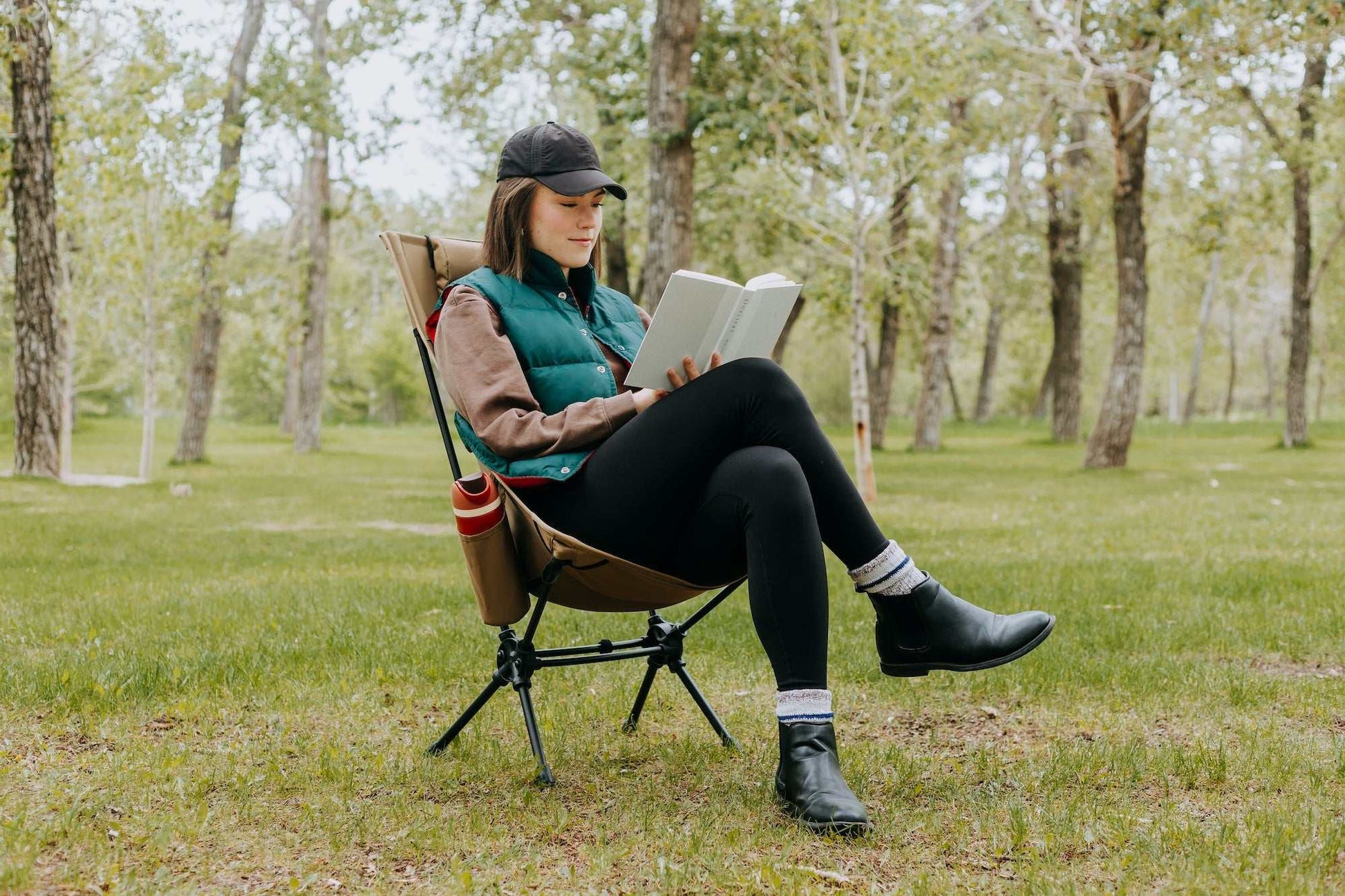 Woman sitting comfortably in a high back ultralight folding camping chair with storage pouches in a forest setting.