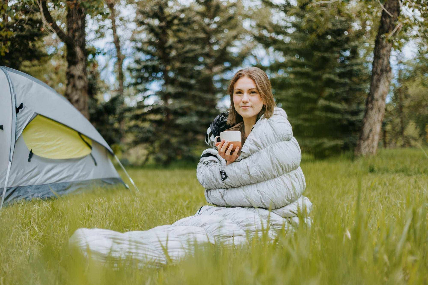 Outdoor camping scene with person in Goose Down Sleeping Bag Grey near a tent.