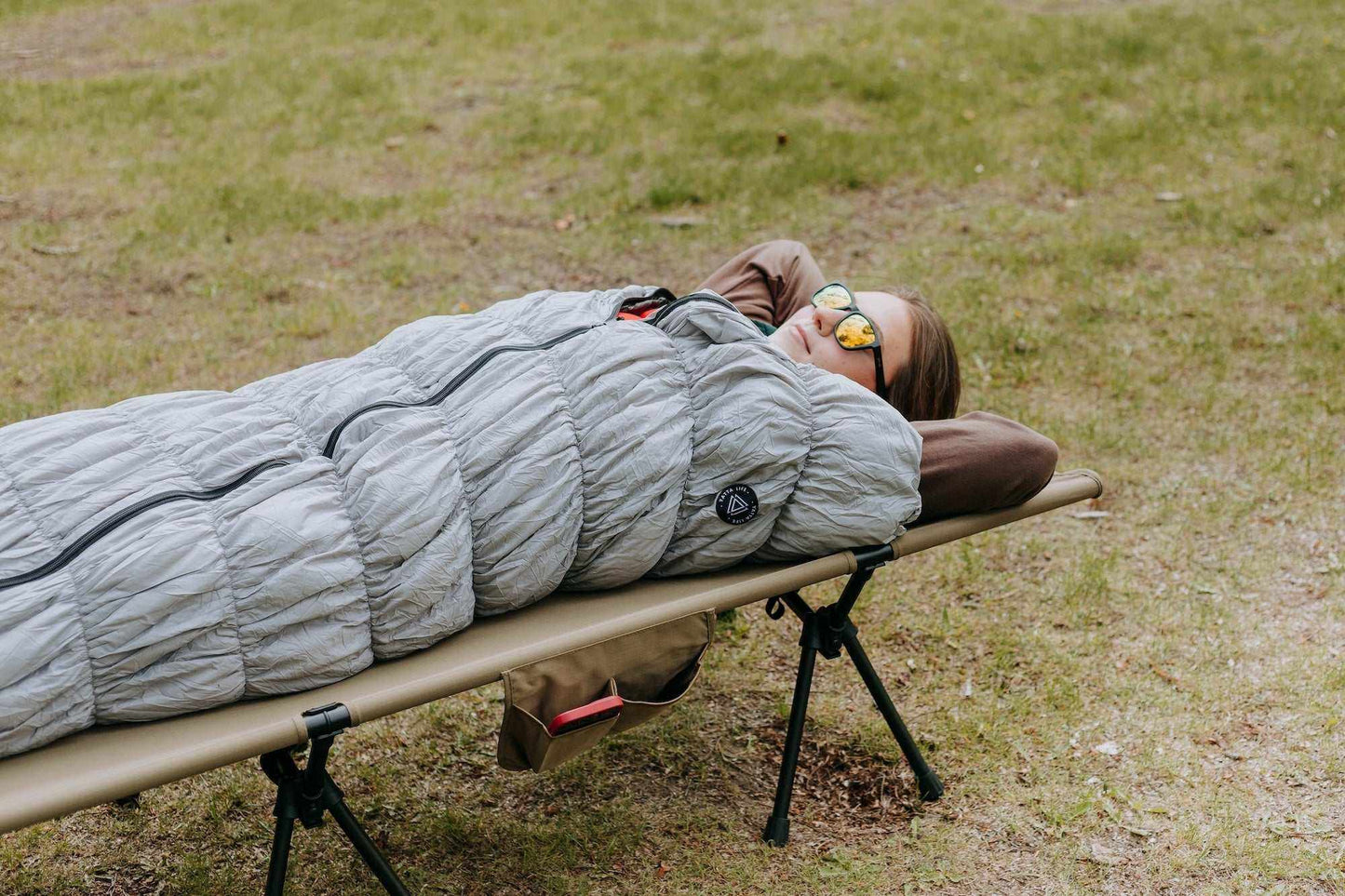 Grey goose down sleeping bag on a portable camping bed outdoors.