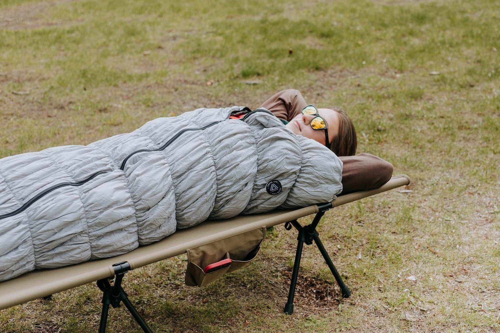Grey goose down sleeping bag on a portable camping bed outdoors.