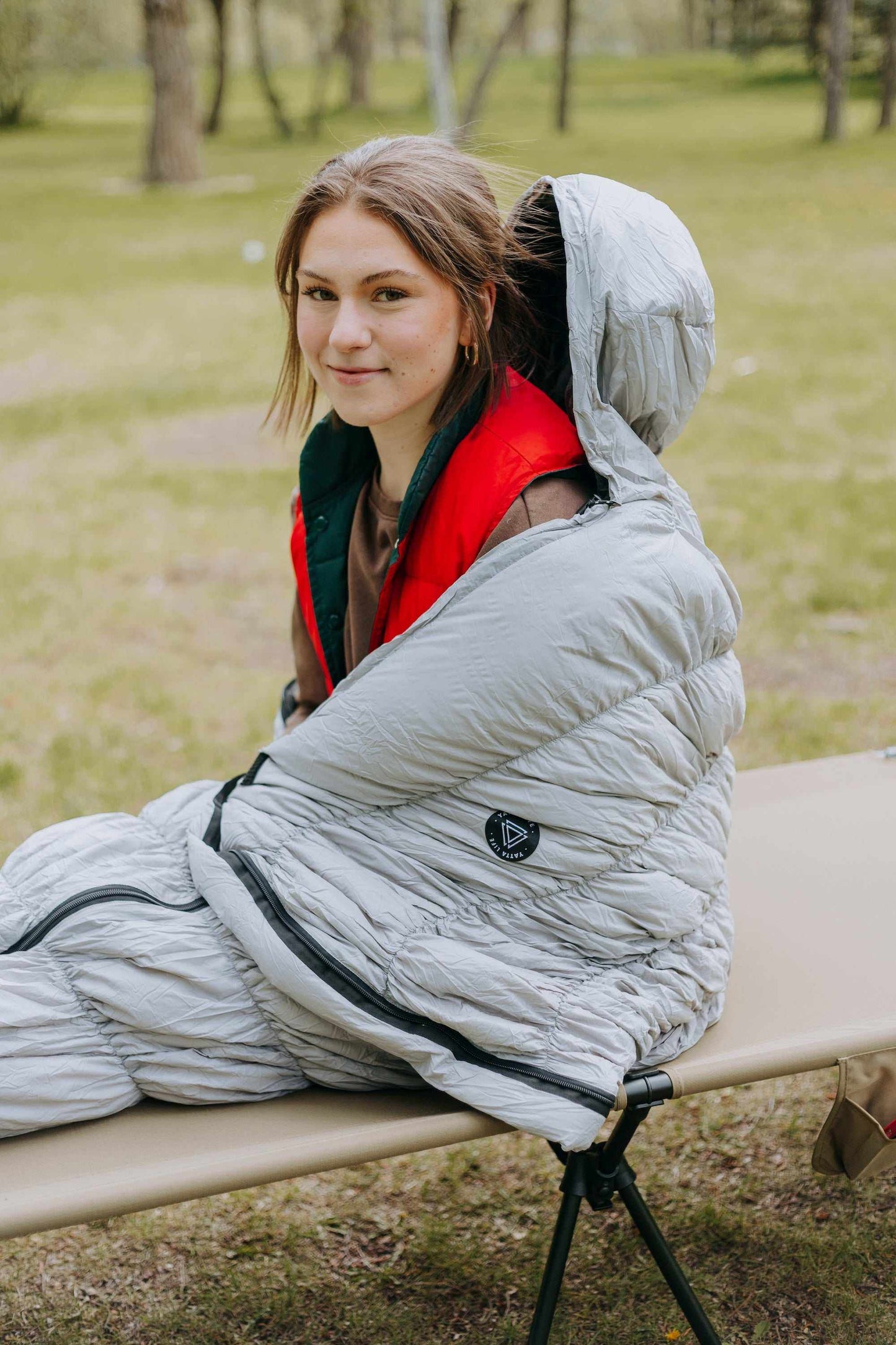 Grey goose down sleeping bag with person sitting inside, showcasing warmth and comfort for outdoor use.