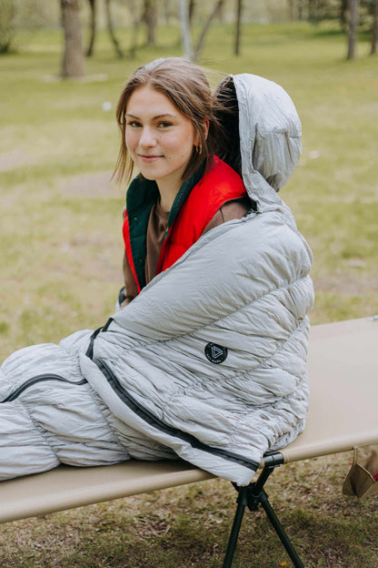 Grey goose down sleeping bag with person sitting inside, showcasing warmth and comfort for outdoor use.