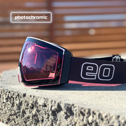 Black ski goggles with rose photochromic lens on stone, outdoor reflection, EO logo strap