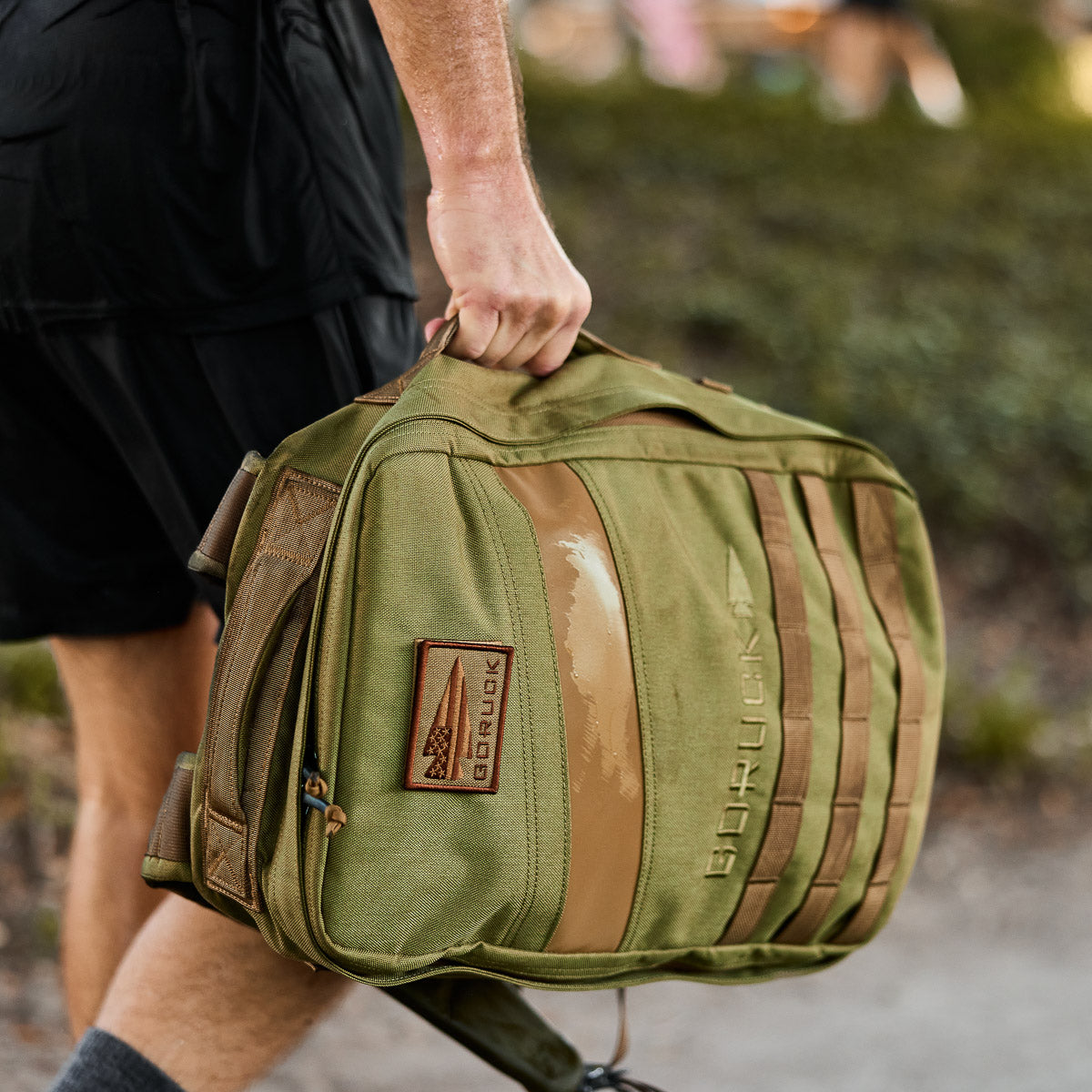 Man carrying olive green GORUCK tactical gym bag outdoors, men's lifestyle gear