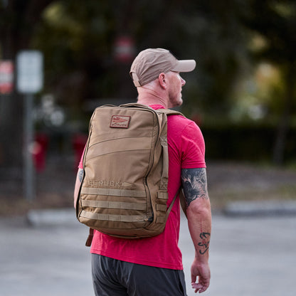 Man outdoors wearing a tan GORUCK Rucker 4.0 backpack, casual athletic outfit, lifestyle gear