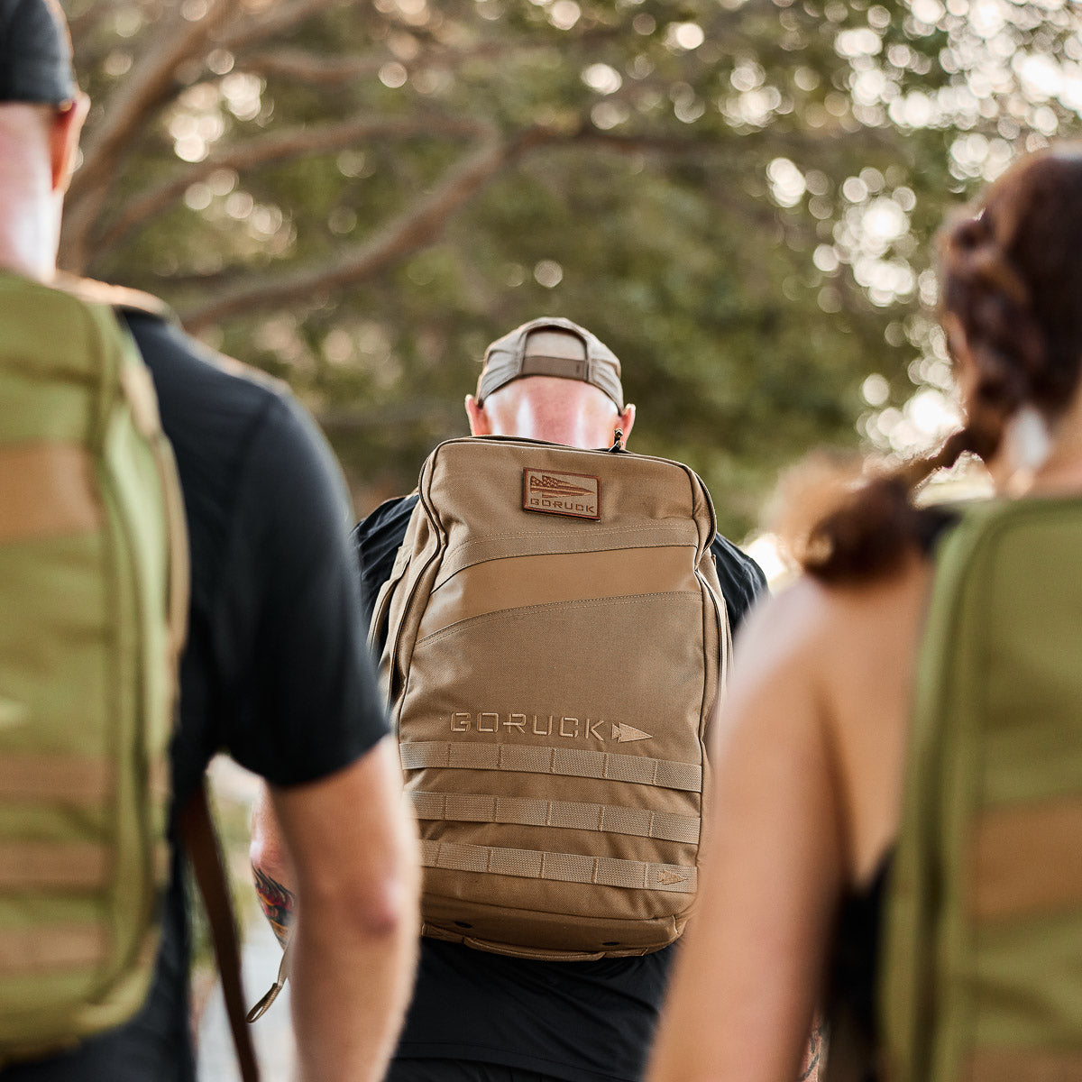 Men wearing GORUCK coyote brown and green backpacks outdoors, curated men's gear.
