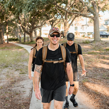 Group of men and women hiking outdoors wearing black shirts, shorts, and tan rucksacks