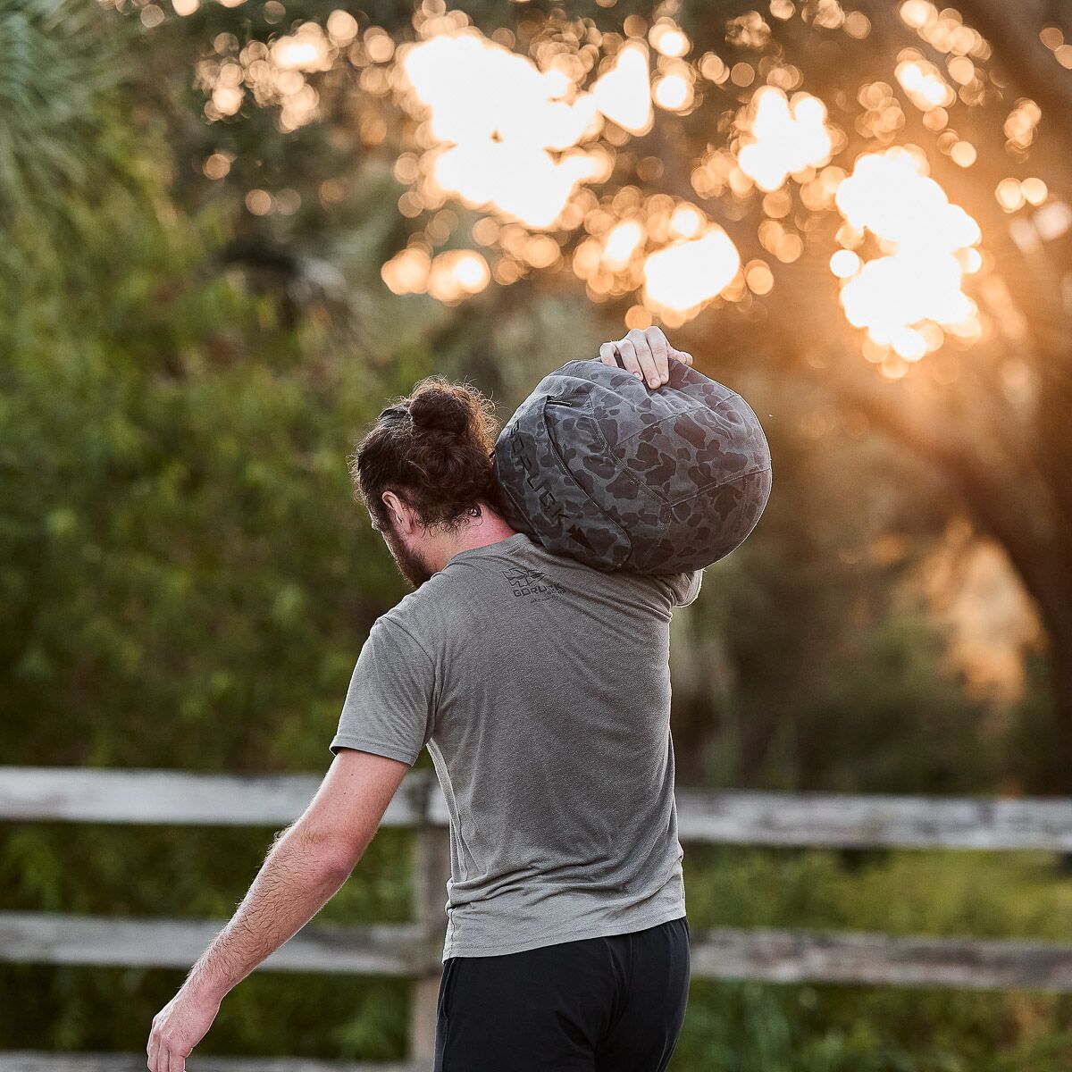 Man carrying camo duffel bag outdoors at sunset, casual active lifestyle for men