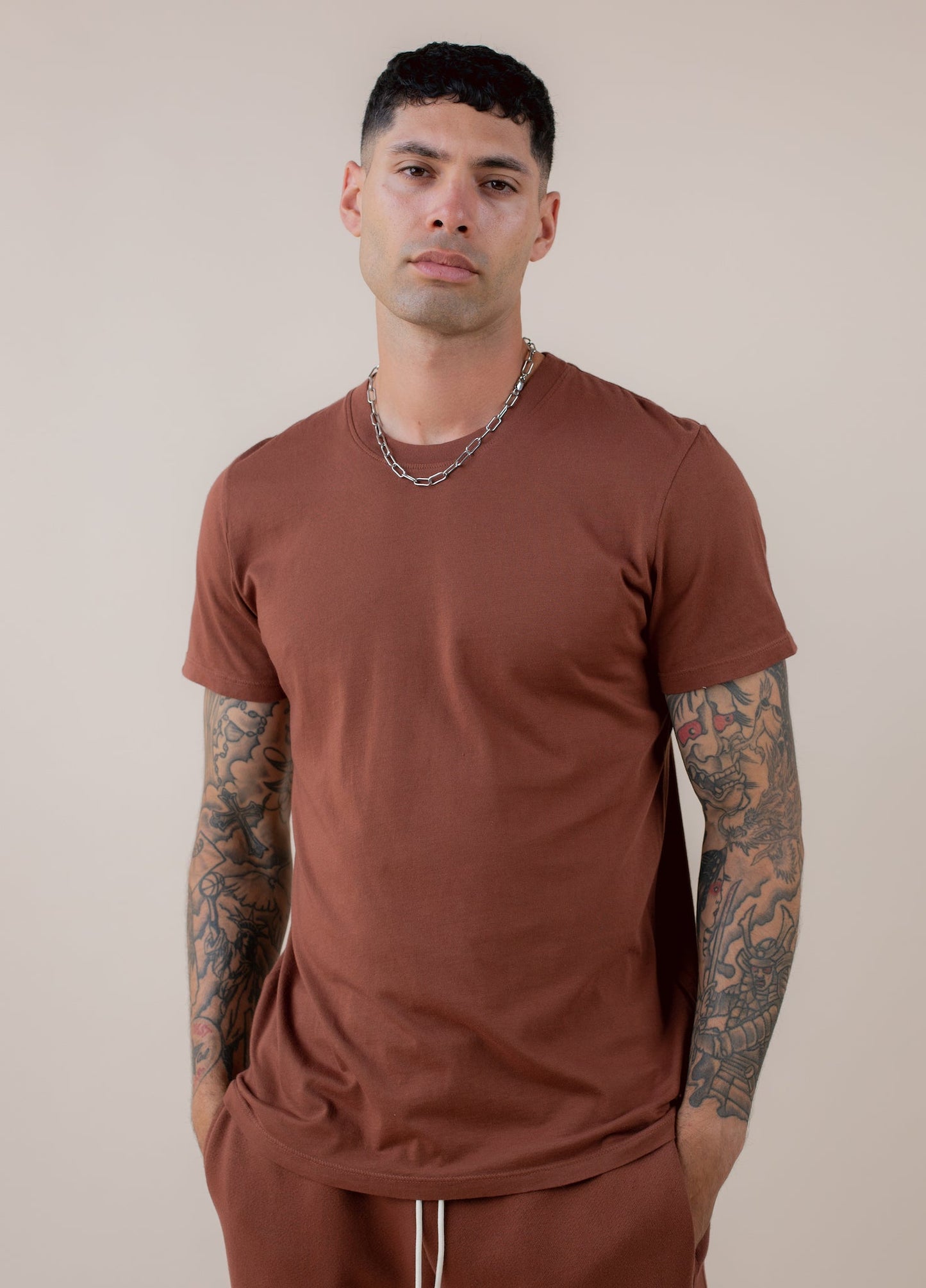 Man wearing a brick-colored basic tee and chain necklace, showcasing men's casual fashion