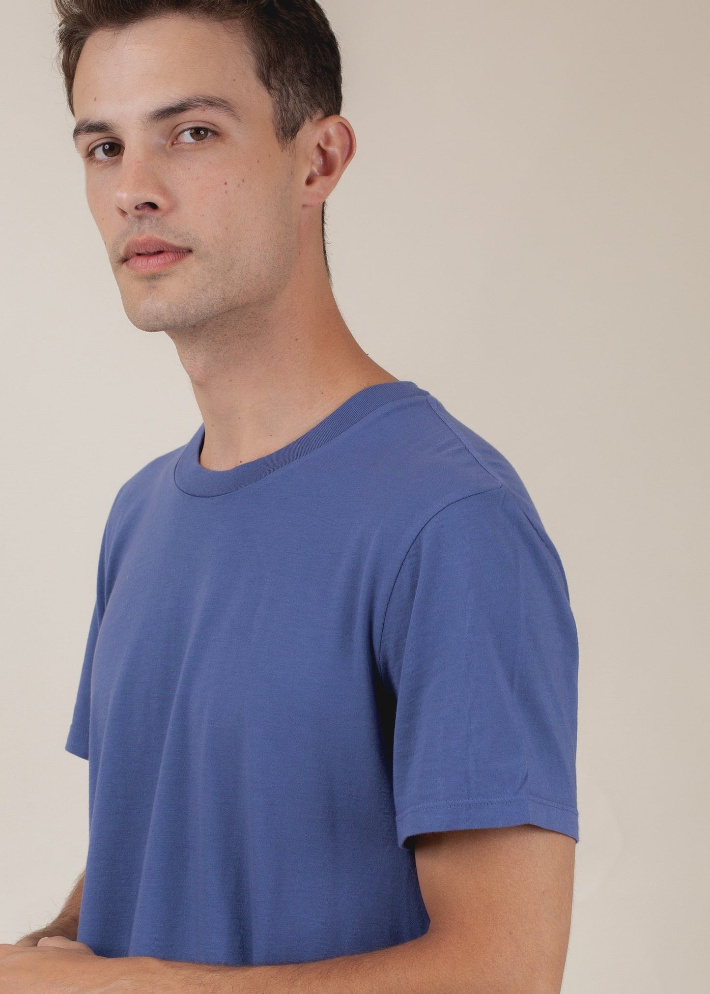 Man wearing a blue basic tee, side view, minimalist background, MANN fashion