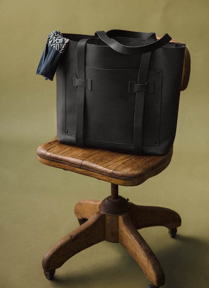 Minimalist black leather tote bag with patterned scarf on wooden chair, men's fashion accessory