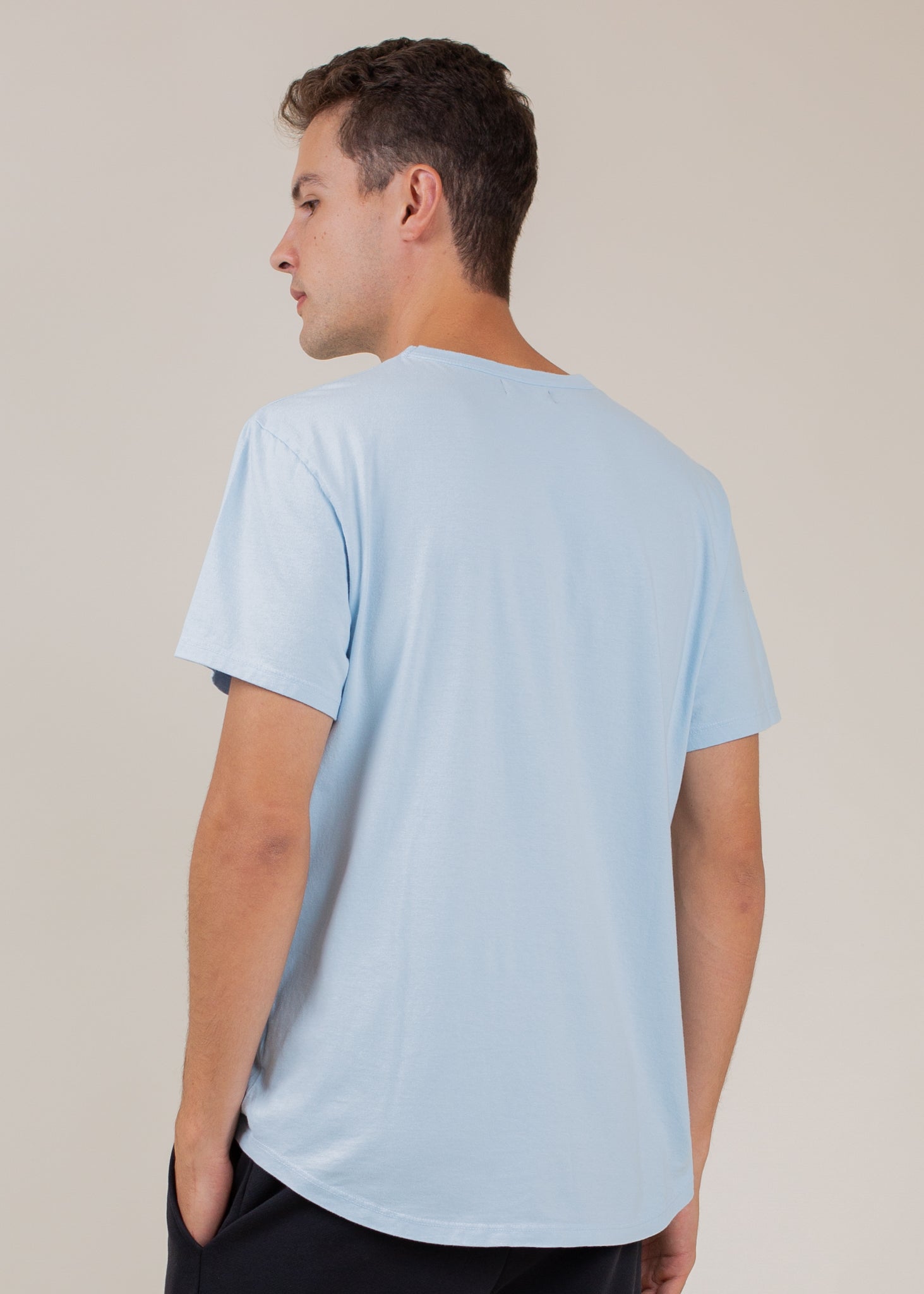Man wearing a sky blue classic tee, seen from the back, minimal background