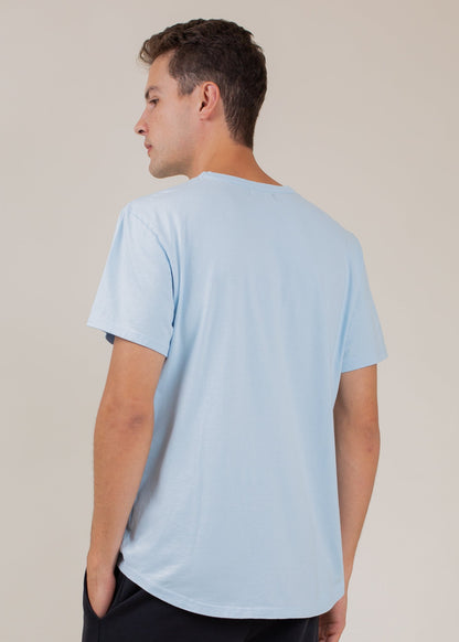 Man wearing a sky blue classic tee, seen from the back, minimal background