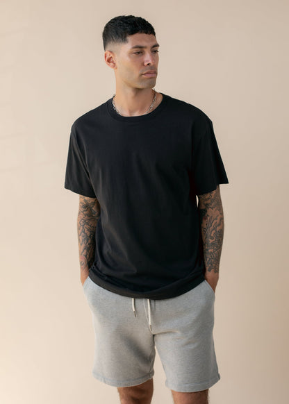 Man wearing black oversized tee and gray shorts, men's fashion on beige background