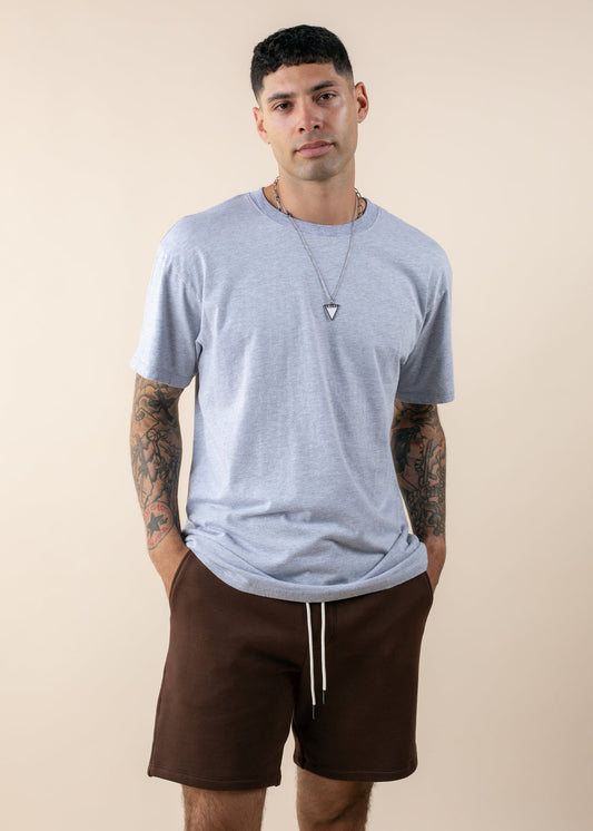 Man wearing oversized heather grey tee and brown shorts, tattoos visible, casual menswear
