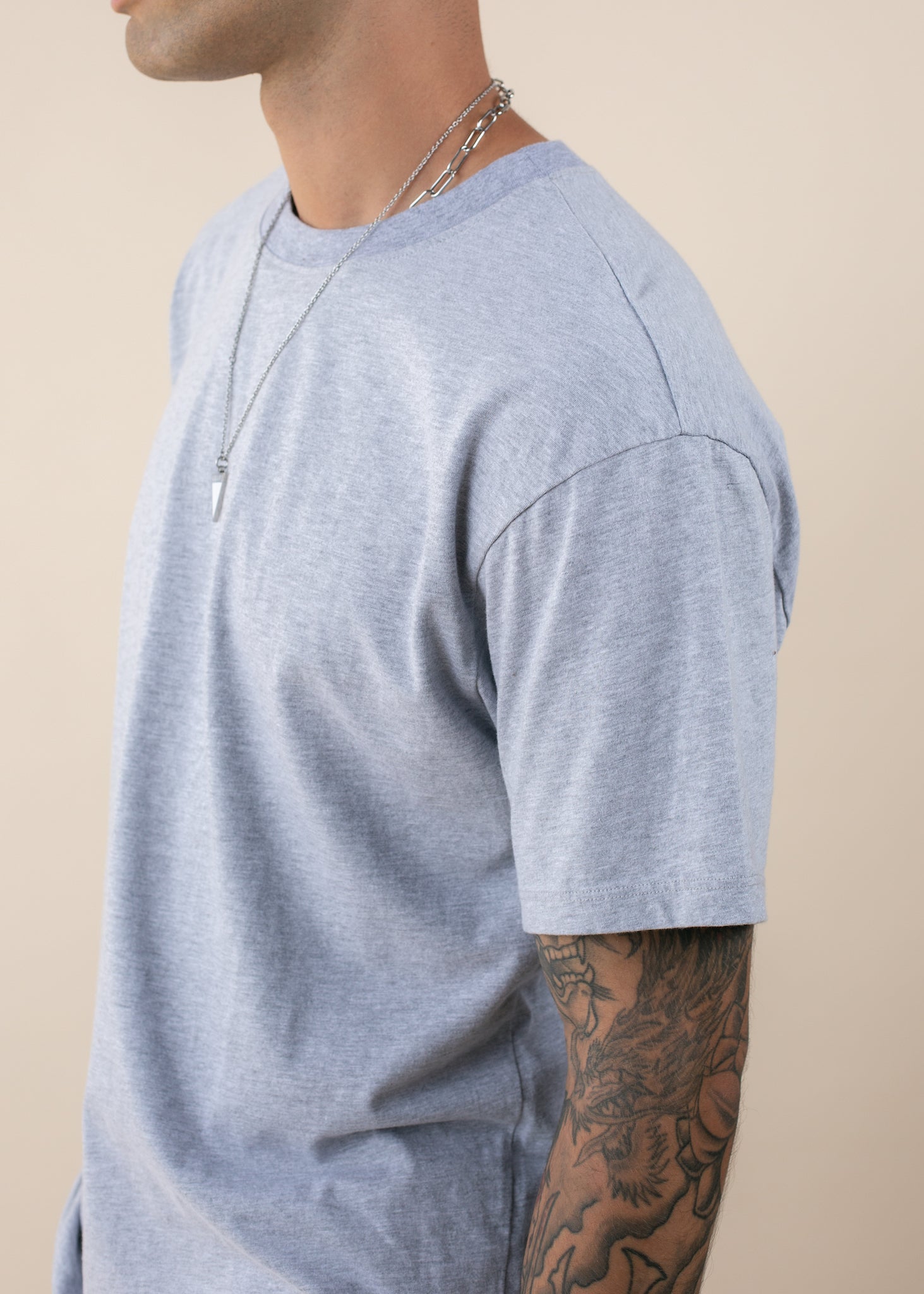 Man wearing a heather grey oversized tee, silver chain necklace, and dragon arm tattoo
