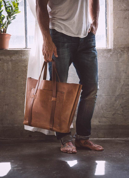 Man in casual jeans and white shirt holding brown leather tote bag, minimalist indoor style