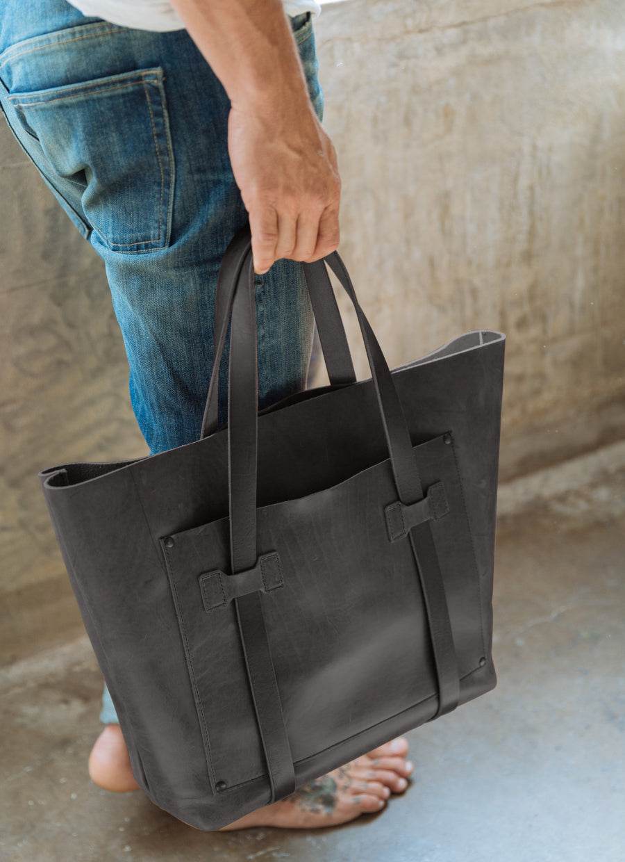 Man in jeans holding black leather tote bag, casual modern men’s fashion accessory