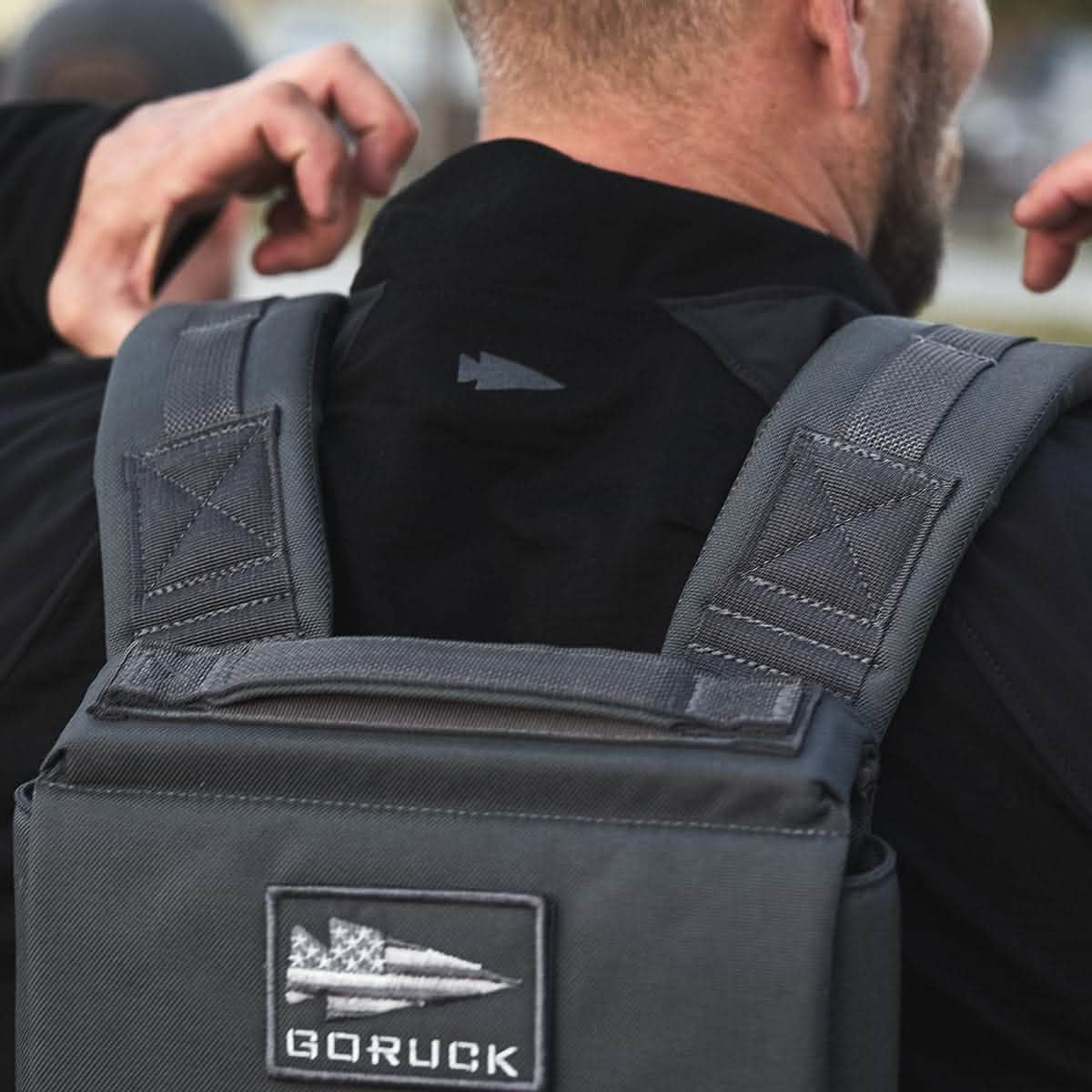 Man wearing a GORUCK grey backpack with American flag patch, outdoors, masculine lifestyle