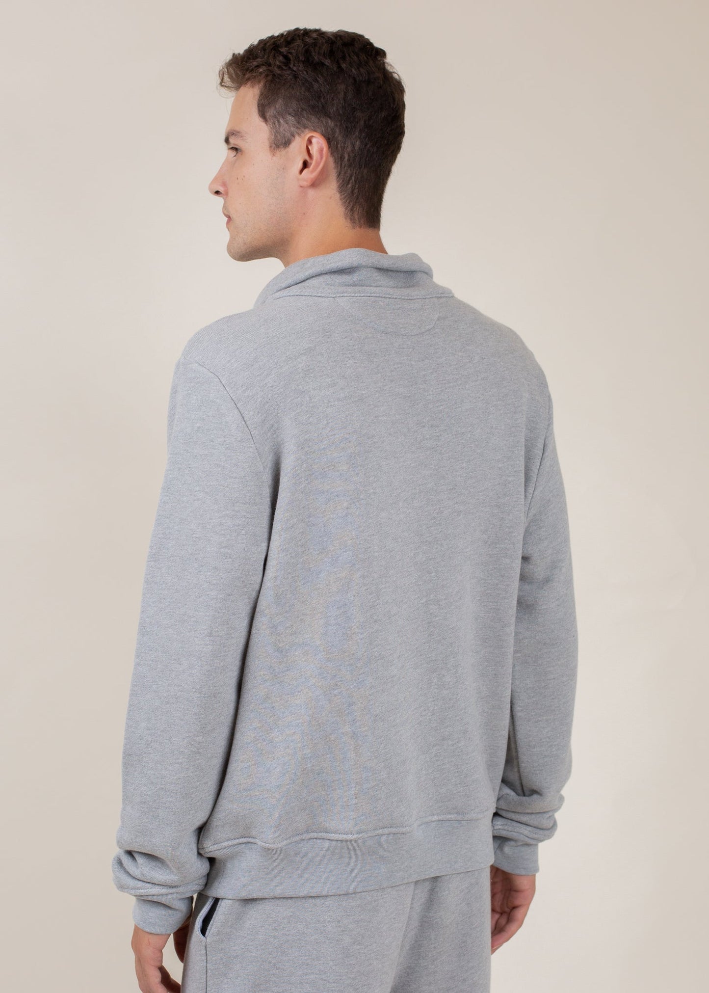 Man wearing light grey half zip sweatshirt and matching sweatpants, back view, neutral background
