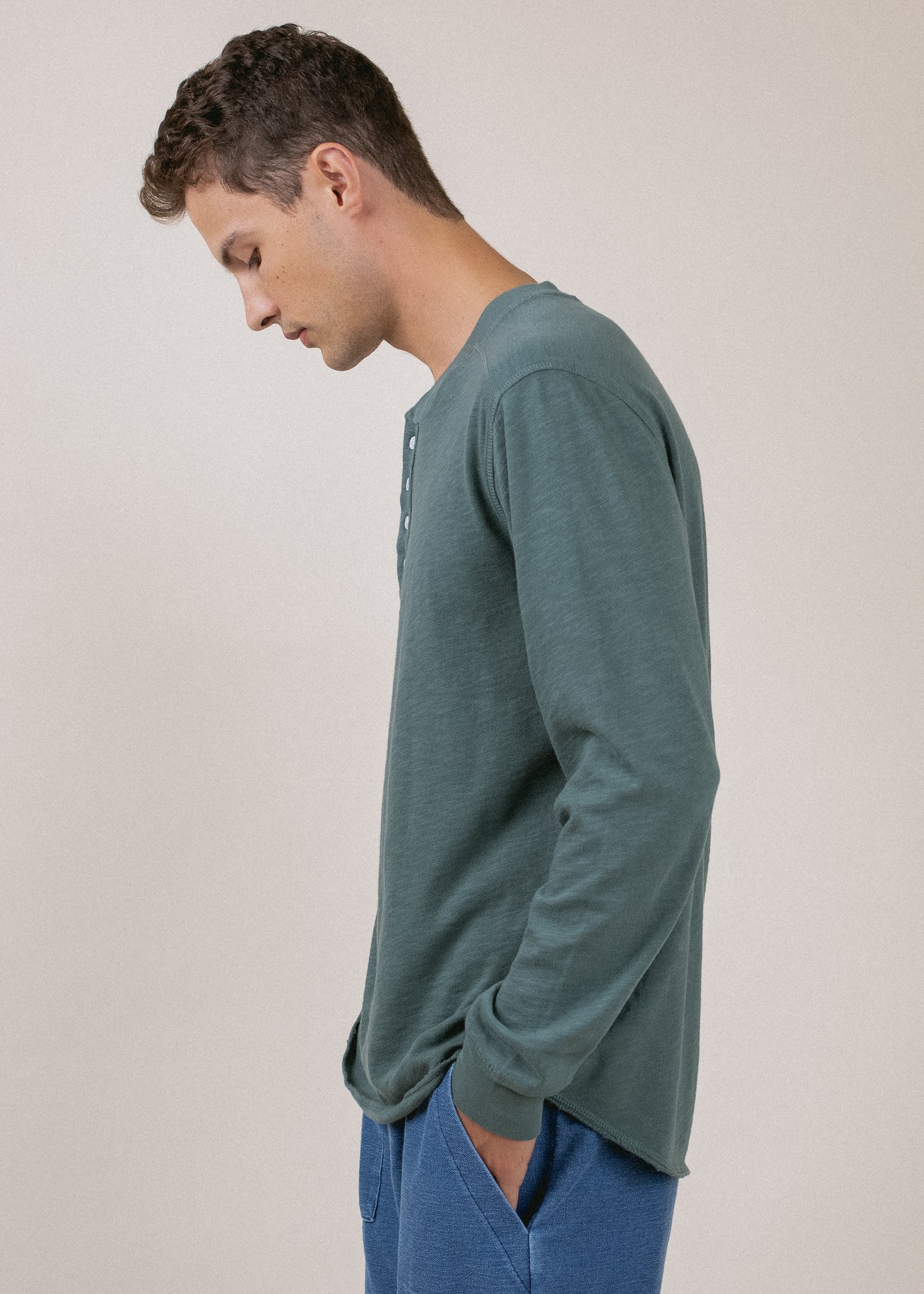 Man in pine green long sleeve henley shirt and blue pants, side view, minimalist background