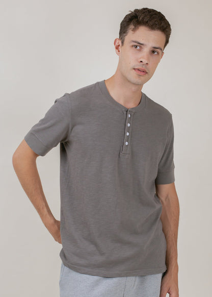 Man wearing cement grey short sleeve henley tee, relaxed fit, minimalist background