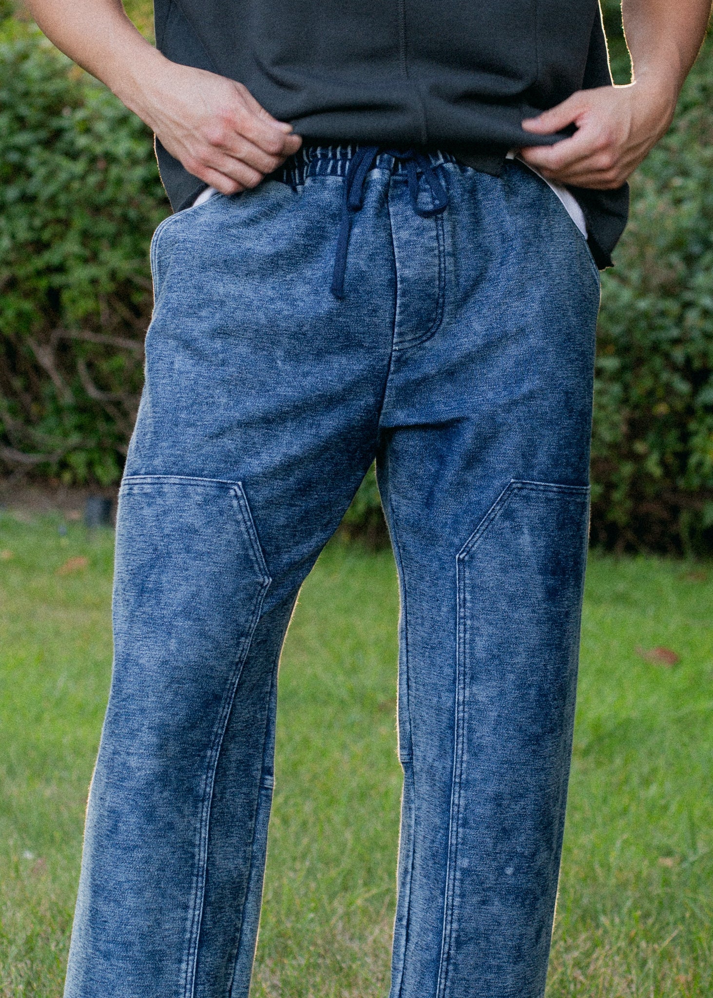Men's indigo patch trousers with drawstring waist, modeled outdoors at MANN marketplace