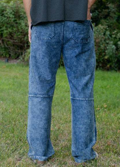 Men's indigo patchwork denim trousers with back pockets, styled outdoors on grass